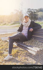 Stylish teenager sitting on a wooden bench on a city street casual wearing