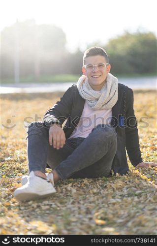 Stylish teenager sitting on the ground in a city park wearing eyeglasses