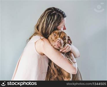 Stylish woman and a charming puppy. Close-up, indoors. Studio photo, white color. Concept of care, education, obedience training and raising pets. Stylish woman and a charming puppy. Close-up