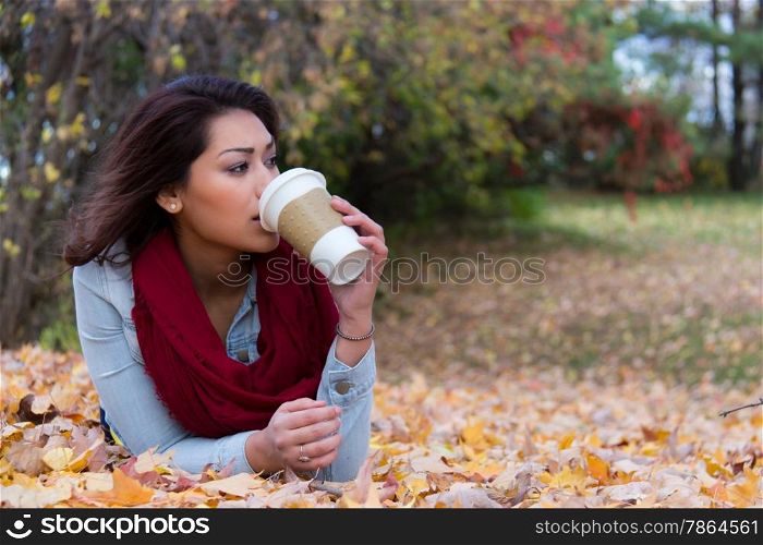 Stylish woman drinking coffee while lying down on fall leaves