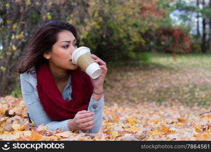 Stylish woman drinking coffee while lying down on fall leaves