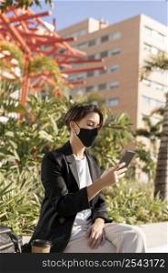stylish woman holding her phone while wearing medical mask