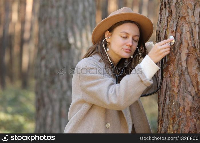 stylish woman in hat listens to a tree with a stethoscope in the forest, concept love the environment.. stylish woman in hat listens to a tree with a stethoscope in the forest, concept love the environment