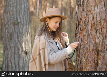 stylish woman in hat listens to a tree with a stethoscope in the forest, concept love the environment. stylish woman in hat listens to a tree with a stethoscope in the forest, concept love the environment.