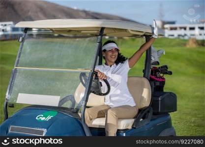 Stylish woman in sportswear driving golf buggy on field and waving with hands greeting friends in sunlight. . Woman in golf cart on field greeting friends