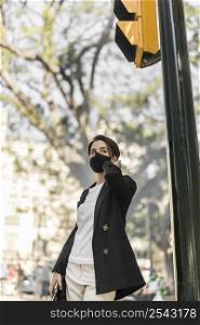 stylish woman talking phone outdoors while wearing medical mask
