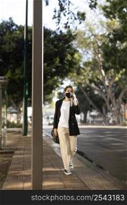stylish woman wearing medical mask outside talking phone