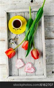 Stylish wooden tray with cup of tea and tulips in romantic style. Morning tea and tulips