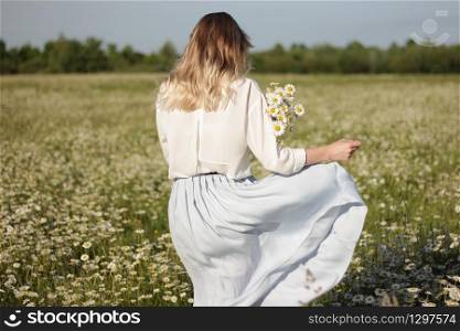 stylish young blonde woman walking in a field with daisies on a sunny summer day. stylish young blonde woman walking in a field with daisies on a sunny summer day.