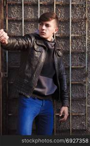 stylish young brunet in leather jacket standing near wallt