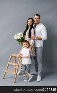 Stylish young family  mom, dad and four-year-old son stand near a wooden stepladder and smile, isolated on a white background. Happy family