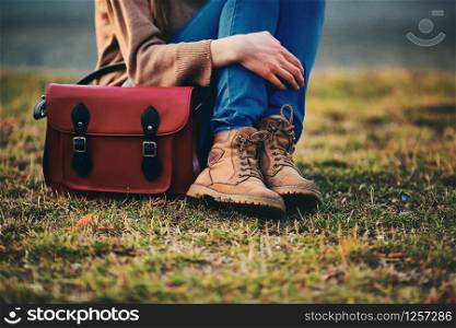 stylish young girl in brown shoes and warm coat sits in the park with a red bag.. stylish young girl in brown shoes and warm coat sits in the park with a red bag