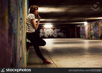 Stylish young girl standing in grunge graffiti tunnel, shanty town. Fashion, trends, subculture. Full body shot