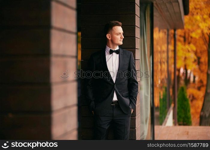 stylish young groom in a black suit in the autumn park on wedding day.. stylish young groom in a black suit in the autumn park on wedding day
