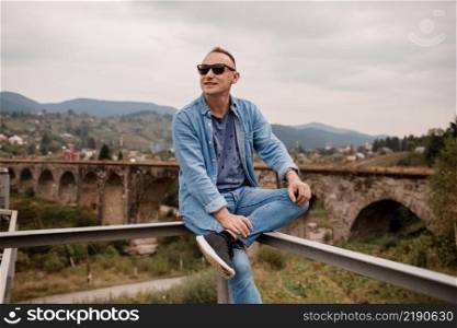 Stylish young man on the railway bridge in Vorokhta, Carpathians against the backdrop of a mountain landscape. tourists sitting in the mountains near the railway.. Stylish young man on the railway bridge in Vorokhta, Carpathians against the backdrop of a mountain landscape. tourists sitting in the mountains near the railway
