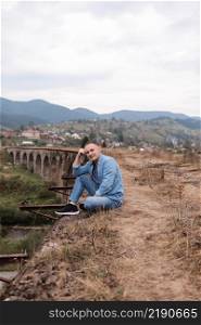 Stylish young man on the railway bridge in Vorokhta, Carpathians against the backdrop of a mountain landscape. tourists sitting in the mountains near the railway.. Stylish young man on the railway bridge in Vorokhta, Carpathians against the backdrop of a mountain landscape. tourists sitting in the mountains near the railway