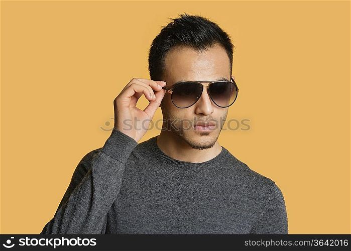 Stylish young man wearing sunglasses over colored background