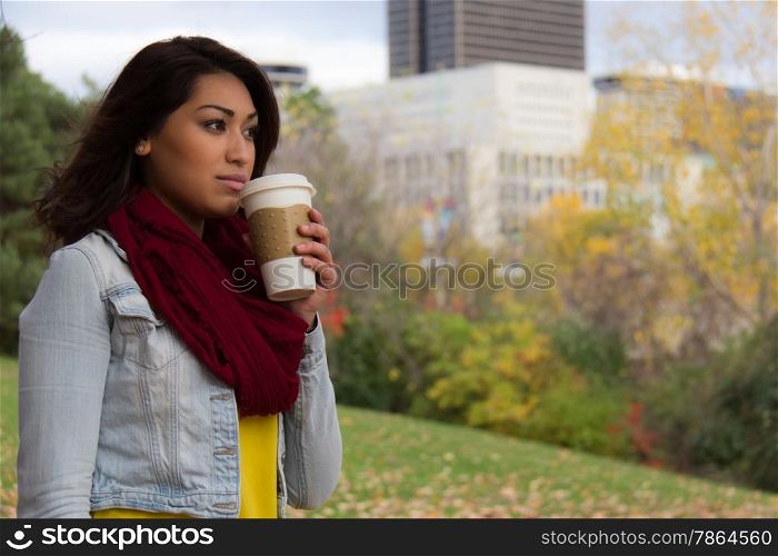 Stylish young woman enjoying coffee during fall with the city in the background