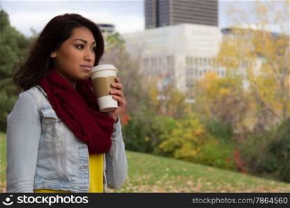 Stylish young woman enjoying coffee during fall with the city in the background