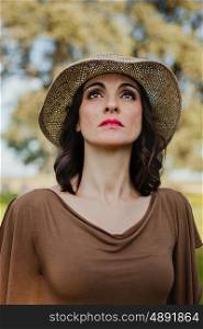 Stylish young woman with straw hat in the field looking up