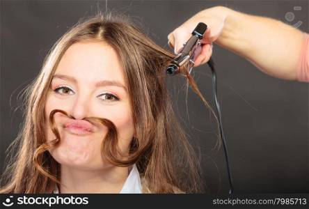 Stylist curling for pretty woman. Girl with hair mustache care about her hairstyle.
