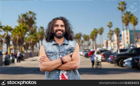 subculture, youth culture and people concept - smiling young hippie man in demin vest over venice beach in los angeles background. hippie man in demin vest at venice beach in la