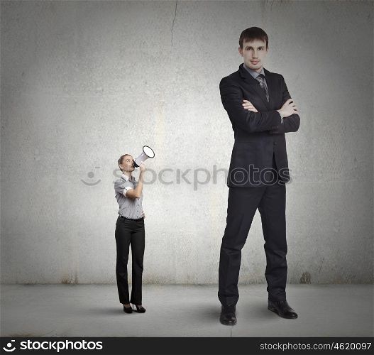 Subordination concept. Small businesswoman screaming in megaphone on colleague of huge size