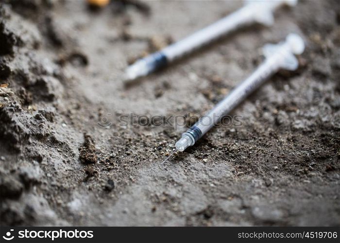 substance abuse, addiction and drug use concept - close up of used syringes on ground