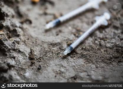 substance abuse, addiction and drug use concept - close up of used syringes on ground