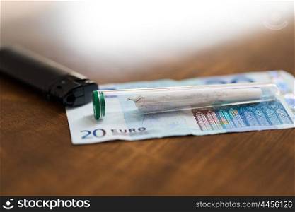 substance abuse, addiction, drug sale and smoking concept - close up of marijuana joint tube, money and lighter on table