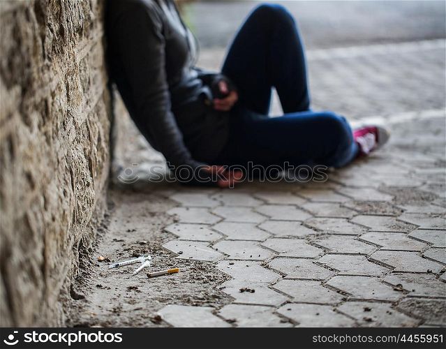 substance abuse, addiction, people and drug use concept - close up of addict woman and used syringes on ground