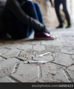 substance abuse, addiction, people and drug use concept - close up of addicts and used syringes on ground