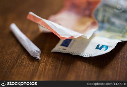substance abuse, nicotine addiction, drug sale and smoking concept - close up of marijuana joint and money
