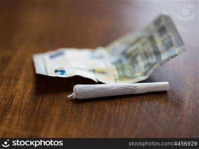 substance abuse, nicotine addiction, drug sale and smoking concept - close up of marijuana joint and money