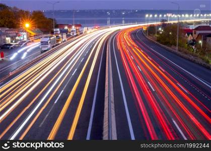 Suburban highway in the evening. Traces from headlights and taillights of heavy traffic and lights on the bridge. Evening Car Traffic With Trails and Truck Parking on the Highway