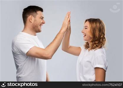 success, achievement and people concept - portrait of happy couple in white t-shirts making high five gesture over grey background. happy couple making high five gesture