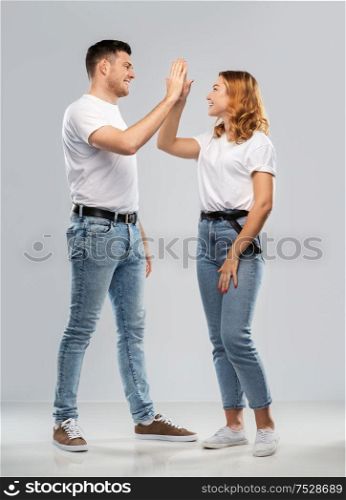success, achievement and people concept - portrait of happy couple in white t-shirts making high five gesture over grey background. happy couple making high five gesture