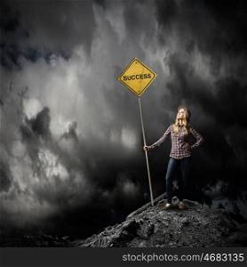 Success ahead. Young woman satnding on rock top with signboard