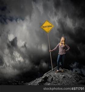 Success ahead. Young woman satnding on rock top with signboard