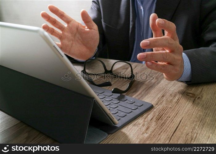 success businessman hand using eyeglass,digital tablet docking smart keyboard on wood desk