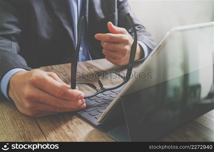success businessman hand using eyeglass,digital tablet docking smart keyboard on wood desk,filter effect