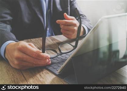 success businessman hand using eyeglass,digital tablet docking smart keyboard on wood desk,filter effect