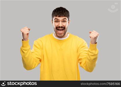 success, emotion and expression concept - happy man in yellow sweatshirt celebrating victory over grey background. happy man in yellow sweatshirt celebrating victory