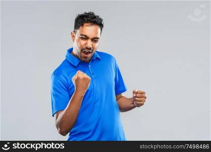 success, emotion and expression concept - happy young indian man celebrating victory over grey background. happy indian man celebrating victory