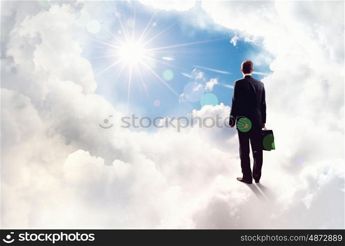 Success in business. Back view of businessman standing on cloud high in sky