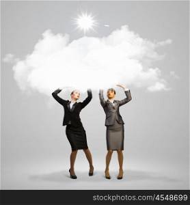 Success in business. Image of two businesswomen holding clouds above head