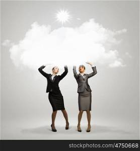 Success in business. Image of two businesswomen holding clouds above head