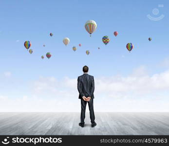 Success in business. Rear view of hopeful businessman looking at balloons flying in sky