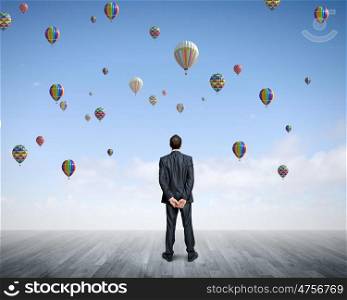 Success in business. Rear view of hopeful businessman looking at balloons flying in sky