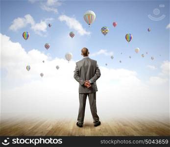Success in business. Rear view of hopeful businessman looking at balloons flying in sky